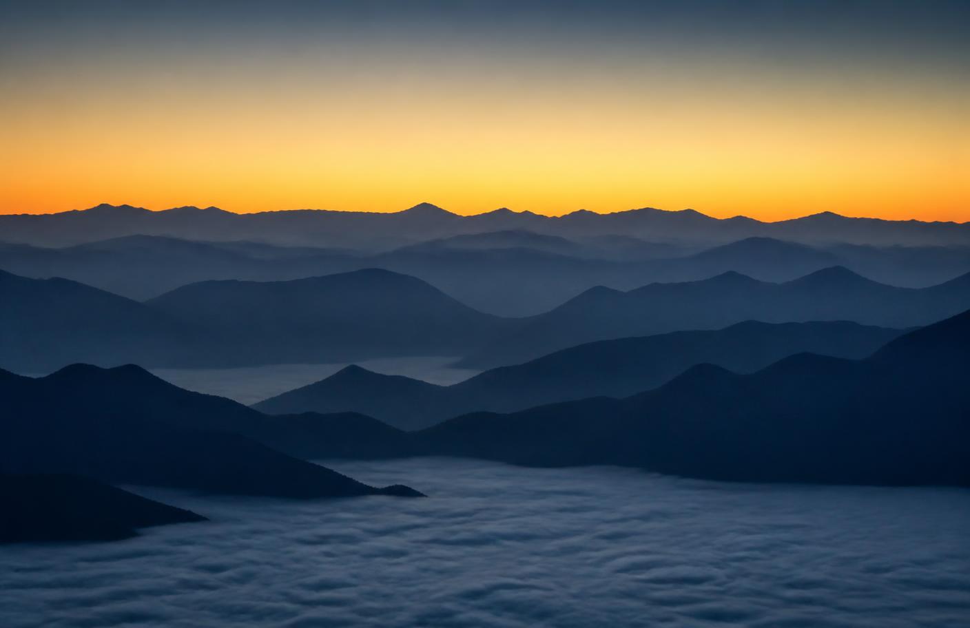 Layered mountain ridges at dawn above cloud cover